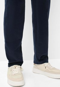 Pantaloni in velluto a coste blu navy con una vestibilità rilassata, caratterizzati da una superficie testurizzata e orli a risvolto coordinati, abbinati a sneakers di colore chiaro.