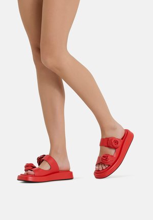 Red sliding sandals with a flat sole, featuring rose-shaped accents and a wide strap. Made of smooth material with a glossy finish.