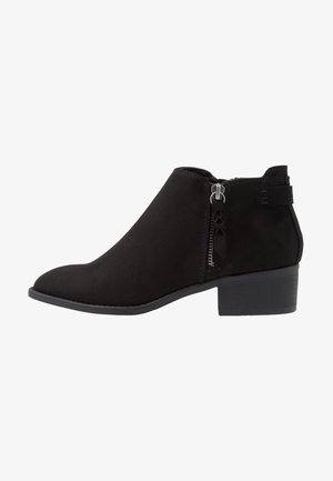 Bota de ante negro hasta el tobillo con cremallera lateral, tacón bajo apilado y puntera redondeada, diseñada para uso casual o formal.
