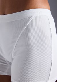 Hvite ribbede bomullsboksershorts med myk elastisk midje og sømløse sider, som viser en fin tekstur og minimalistisk design.