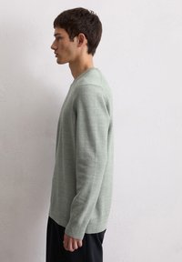 Pull vert clair à manches longues, tricot texturé et col rond, associé à un pantalon noir. Design simple et tissu doux.
