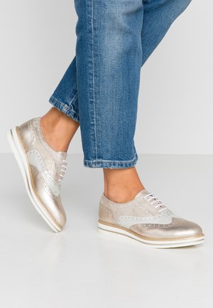 Lyse metallic sølv snøresko med perforerede detaljer og en kontrasterende lyseblå sektion. Flad hvid sål og glat tekstur.
