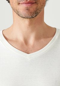 Witte V-hals T-shirt gemaakt van een zachte, geribbelde stof. De halslijn heeft een gladde, contrasterende afwerking. Subtiele textuur is zichtbaar.