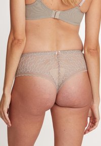 Beige hipsterondergoed van kant met een bloemenpatroon, voorzien van een scalloped rand en een klein knoopdetail aan de achterkant.