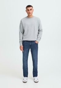 Hanorac gri, blugi din denim albastru și adidași albi pe o persoană. Hanoracul are guler rotund; blugii au o croială clasică și un ton închis.