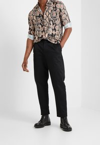 Kraťasová košile s černým a béžovým hadím vzorem, spárovaná s černými zúženými kalhotami a černými šněrovacími botami. Hladká, lehká tkanina.