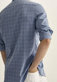 Chemise à carreaux bleue en tissu léger avec une texture douce, dotée de manches retroussées et d'un ourlet incurvé.