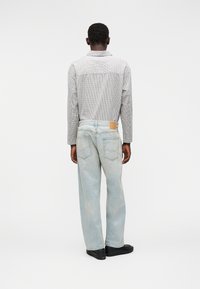 Καρό πουκάμισο με κουμπιά σε μαύρο και λευκό, συνδυασμένο με τζιν τζιν σορτς σε ανοιχτό μπλε, με μια δερμάτινη ετικέτα στη πίσω μέση.