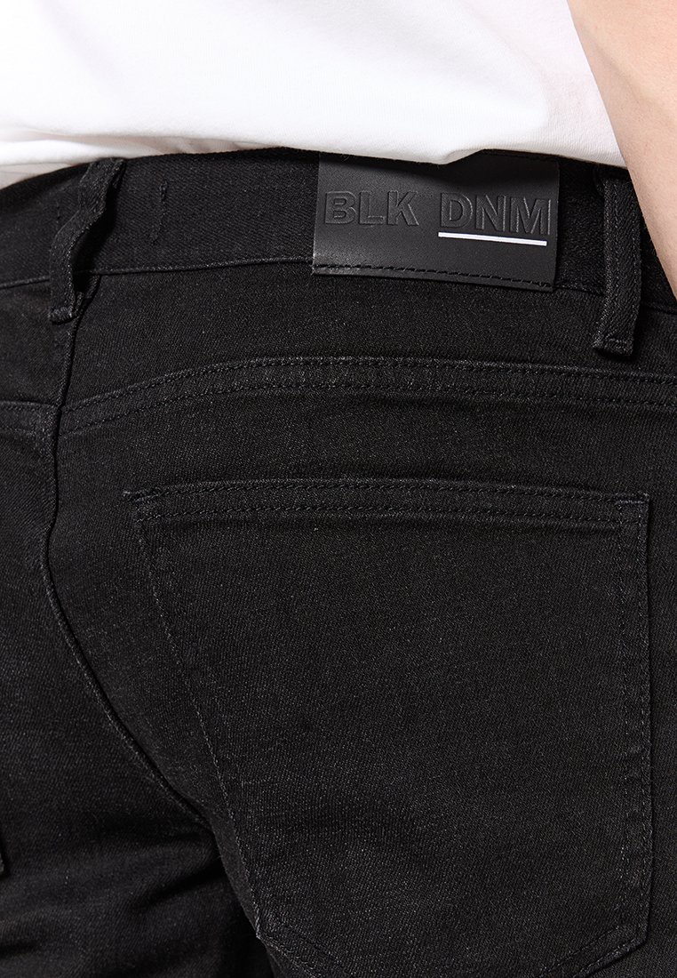 Schwarze Denim-Jeans mit einem Lederlabel mit der Aufschrift "BLK DNM" am Bund, ausgestattet mit normalen Gesäßtaschen und einer eleganten, glatten Textur.