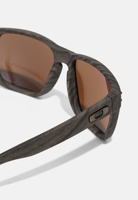 Ochelari de soare cu model gri și lentile tonificate în maro, având un design texturat al ramei și accente metalice pe tâmple.
