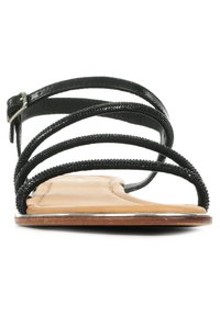 Sandalo nero con cinturini e decorazioni a perline, suola piatta color cammello, cinturino alla caviglia regolabile e design open toe. Texture in pelle liscia.