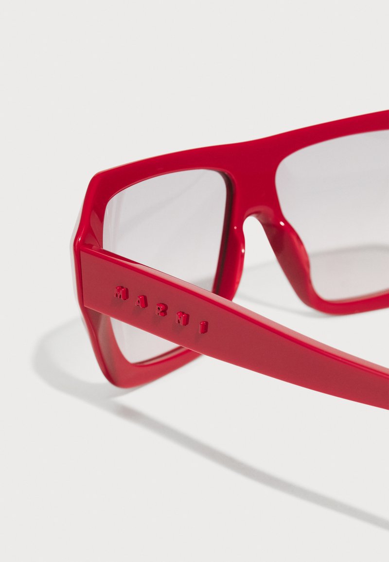 Rote Plastiksonnenbrille mit quadratischer Form und dicken Rahmen. Transluzente Gläser. "Marni" in das Gestell eingeprägt. Glatte Oberfläche.