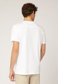 T-shirt bianco a maniche corte con scollatura rotonda, realizzato in cotone. Presenta una texture liscia e una vestibilità rilassata, indossato con pantaloni beige.