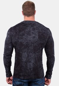 Langärmliges schwarzes Shirt mit einem strukturierten, marmorierten Design. Figurbetonte Form, runder Halsausschnitt und weicher Stoff. Kombiniert mit blauen Jeans.