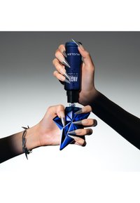 Blauer sternförmiger Parfümflakon, der mit einer Hand gehalten wird, während eine blaue zylindrische Sprühflasche mit eleganten metallischen Akzenten darüber positioniert ist.