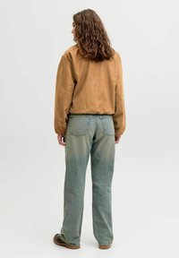 Brun oversized skjorte i ruskind kombineret med lyseblå denimjeans med en falmet gradient effekt, løs pasform og baglommer.