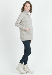 Vaaleanharmaa pooloneule, jossa on ribbireunat ja napilliset hihansuut, yhdistettynä tummiin legginsseihin ja beigeihin nauhakenkiin.