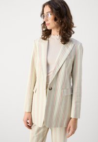 Blazer a righe in colori pastello (rosa, verde, bianco) con lapel a punta, chiusura con un solo bottone e tasche frontali; abbinato a un top a coste.