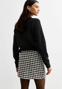 Zwarte trui gecombineerd met een geruite rok in zwart-witte kleuren. De stof is zacht en de rok is kort met een getailleerd ontwerp.
