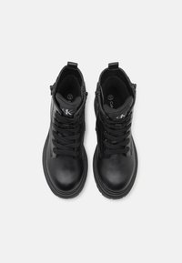 Sorte lær ankelsko med teksturert overflate, rund tå og snørelukking. Har glidelås på siden og logo på tungen.