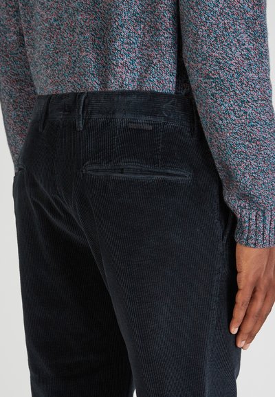 Czarne spodnie z kordurowej tkaniny o prążkowanej teksturze, z dwiema tylnymi kieszeniami i subtelną metką, w połączeniu z kolorowym swetrem dzianym.