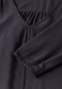 Blusa blu scuro con scollatura a V, dettagli arricciati e maniche lunghe con polsini elasticizzati. Il tessuto presenta una texture e un motivo delicati.