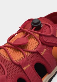 Αναπνεύσιμο αθλητικό παπούτσι σε κόκκινο και πορτοκαλί χρώμα με ελαστικό σύστημα κορδονιών και μαύρο κούμπωμα για γρήγορη προσαρμογή.