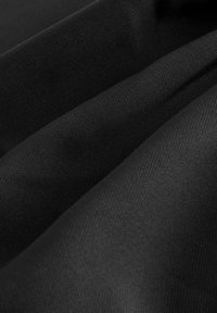 Gros plan de plis de tissu noir lisse montrant une texture de tissage fine et un drapé doux.