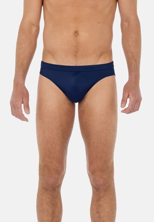 Slip da nuoto della marina realizzati in un tessuto liscio e elasticizzato, con un taglio a vita bassa e una fascia larga in vita. Nessun motivo o accento visibile.