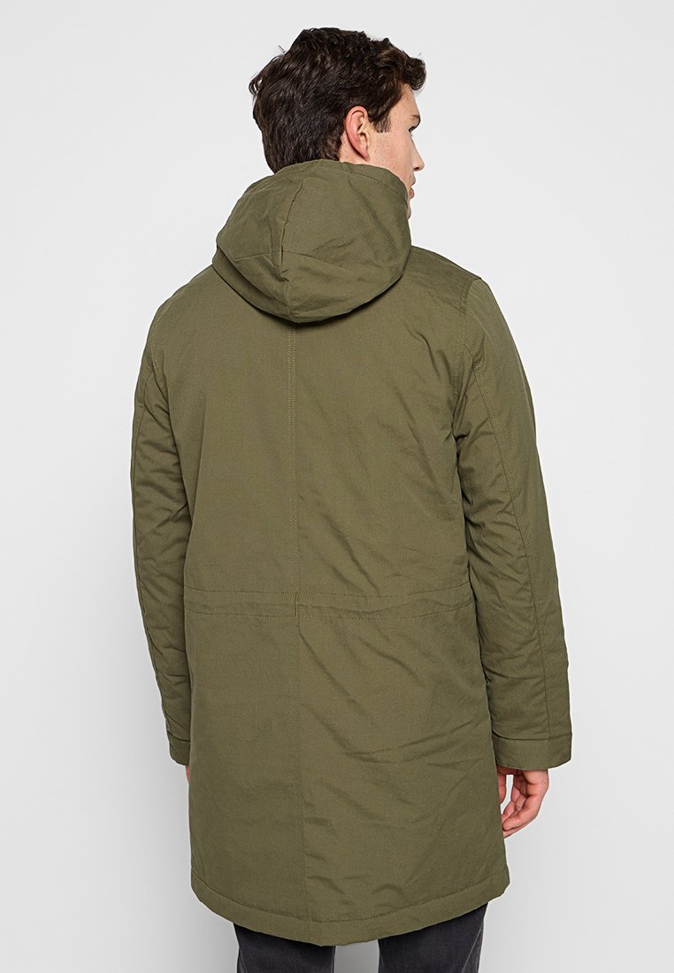 Parka con capucha de color verde oliva con un diseño de longitud media, fabricada en tejido suave, que presenta un corte recto y detalles de costura visibles.
