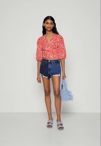 Piros virágmintás crop top puffos ujjakkal, magas derékú farmer rövidnadrággal párosítva. Kiegészítők között egy világoskék, bolyhos kézitáska és hozzáillő szandálok találhatók.