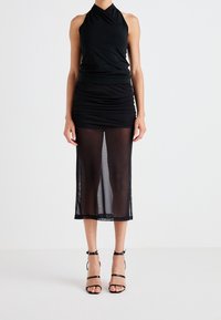 Schwarzes Halftertop kombiniert mit einem schwarzen gerafften Minirock mit durchsichtiger Überlage. Das Model trägt strappy schwarze High Heels.