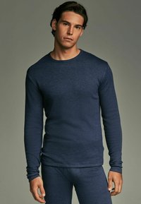 Tummansininen pitkähihainen termopaita, jossa on pyöreä kaula-aukko, teksturoitu kangas, slim fit -malli ja yhteensopivat housut, neutraalilla taustalla.