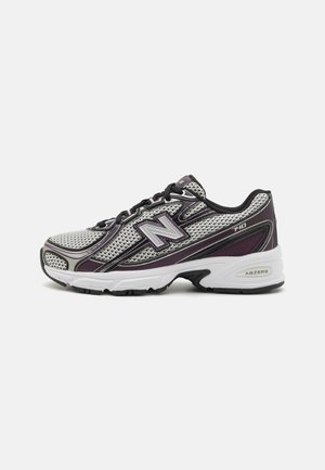 Zapatilla deportiva New Balance gris y morada con cordones negros y suela blanca, modelo 740, mostrada de lado sobre fondo blanco.