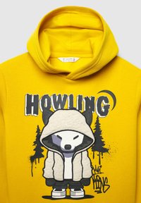 Felpa gialla con un lupo dei cartoni animati che indossa una felpa bianca. Il design include il testo "HOWLING" e silhouette di alberi neri. Texture morbida.