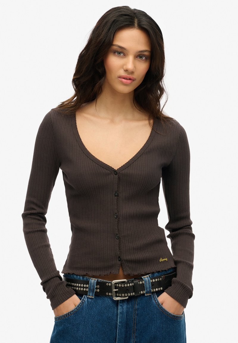 Brun ribbet langærmet cardigan med V-udskæring, knaplukning og råd kant. Båret med et sort nitterbælte og blå højtaljede jeans.