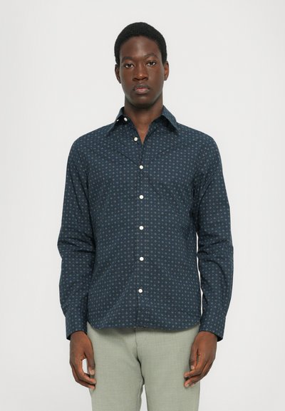 Chemise boutonnée marine avec un motif géométrique, en tissu léger. Présente un col classique et des boutons blancs sur fond sombre.