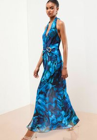 Pitkä sininen kukallinen mekko, jossa on halterneck-olkaimet, kietaisuyksityiskohta vyötäröllä ja sydämen muotoinen metallikoriste. Silkkinen kangas.