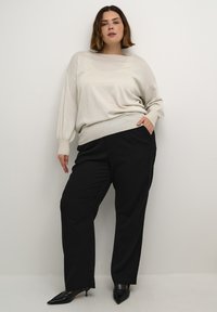 Pull en tricot texturé gris clair avec une coupe décontractée et des épaules tombantes, associé à un pantalon noir à jambes larges et des escarpins noirs à bout pointu.