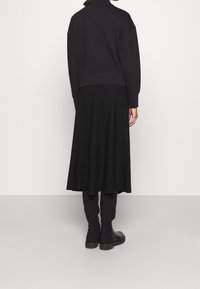 Sweat-shirt noir à col montant et épaules tombantes, associé à une longue jupe noire fluide, porté avec un pantalon slim noir et des bottines.