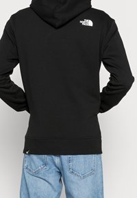 Felpa con cappuccio in misto cotone nero, con logo bianco sul retro, orlo a coste e maniche lunghe abbinate a jeans azzurri chiari.