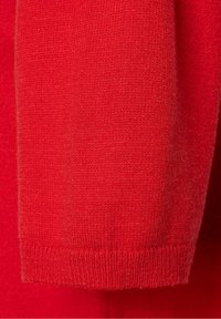 Czerwony dzianinowy materiał o miękkiej teksturze, z prążkowanym mankietem. Bezszwowy fason ukazuje równomierny splot na całej długości.