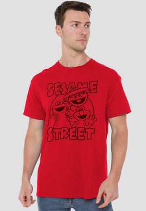 Red cotton t-shirt featuring black graphic print of three Sesame Street characters and the words "SESAME STREET." Classic crew neck design.