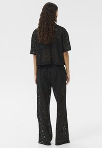 Ensemble deux pièces en dentelle noire comprenant un haut court à manches courtes et un pantalon ample, présentant des motifs géométriques découpés.