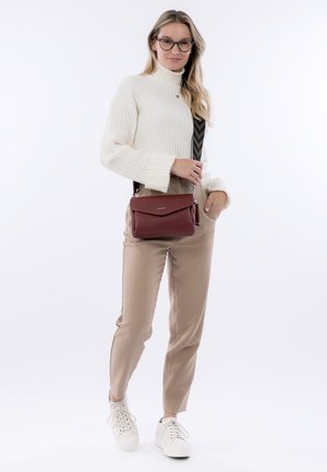 Bolso cruzado de cuero texturizado rojo con cierre magnético, combinado con un suéter de cuello alto de canalé blanco y pantalones ajustados beige.