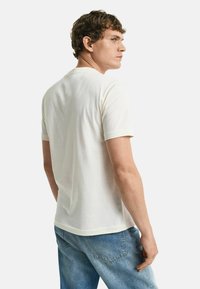 Camiseta de manga corta color crema hecha de algodón, con un clásico cuello redondo y un corte recto, combinada con jeans de mezclilla azul claro.