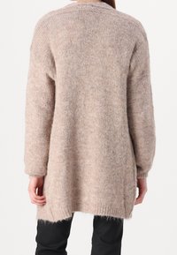 Długi, oversizeowy beżowy sweter wykonany z miękkiego, teksturowanego dzianinowego materiału. Posiada opuszczone ramiona i ściągacze na rękawach, prosty dół oraz boczne rozcięcia.