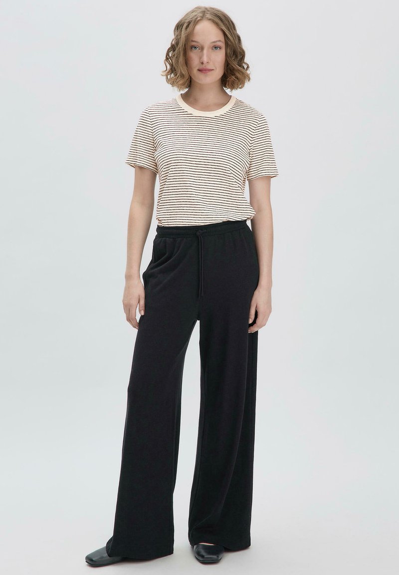 Gestreepte t-shirt met korte mouwen in beige en bruin, gecombineerd met zwarte wijde broek. De outfit heeft een ontspannen pasvorm en een elastische tailleband.