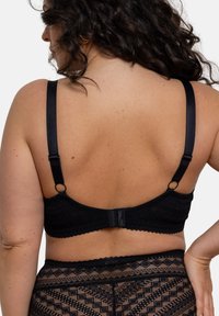 Soutien-gorge en dentelle noire avec des bretelles ajustables, présentant un motif texturé et une fermeture à crochets au dos. Détails accentués sur le bandeau.