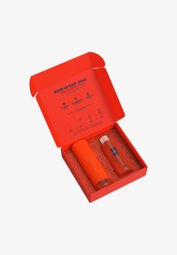 Rode doos met oranje binnenkant bevat een geribbelde oranje sprayfles en een doorzichtige oranje vloeistofcontainer, beide gelabeld met blauwe tekst.